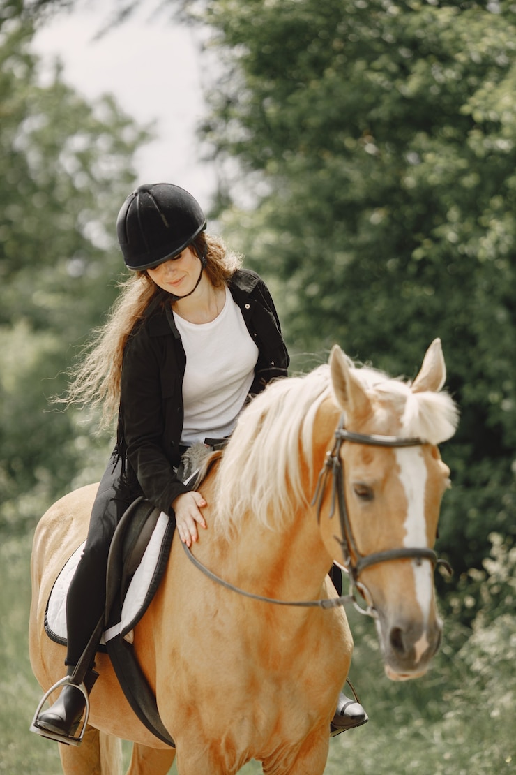 Zdarma Fotografie rider woman riding her horse on a ranch. woman has long hair and black clothes. female equestrian touching her brown horse.