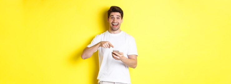 Zdarma Fotografie šťastný muž ukazuje na smartphone, aby ukázal propagační nabídku internetu, stojí na žlutém pozadí
