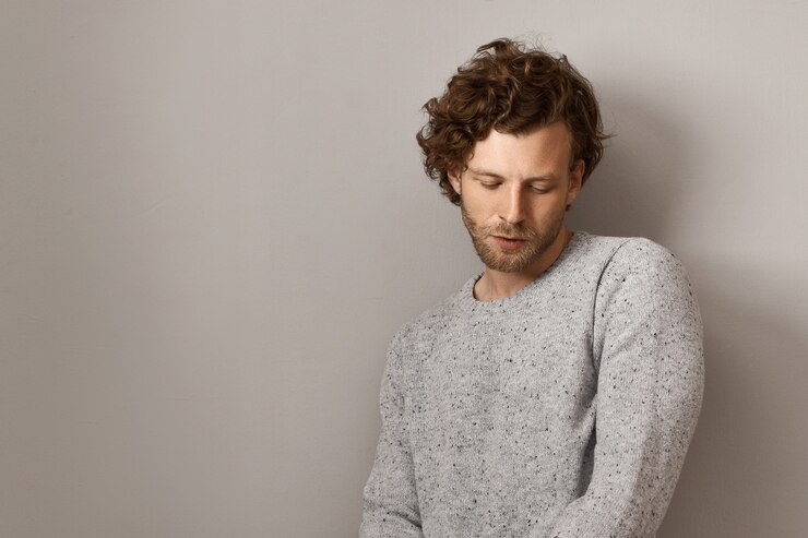 Zdarma Fotografie stylish handsome young european man with trimmed beard and voluminous reddish hair dressed in cozy warm gray sweater, looking down with shy timing facial expression, thinking about something