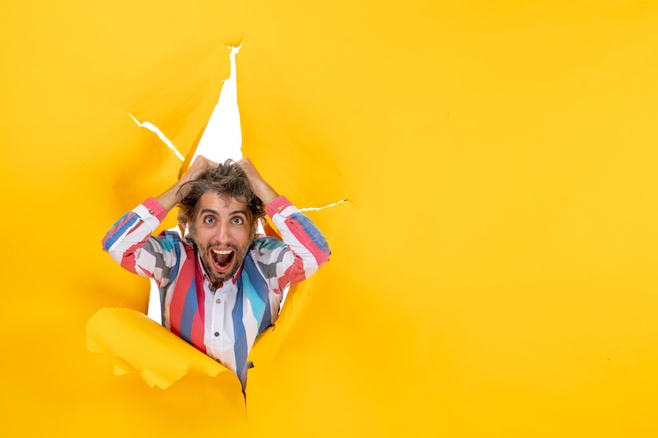 Zdarma Fotografie top view of an emotional overtired and exhausted young guy through a torn hole in yellow paper