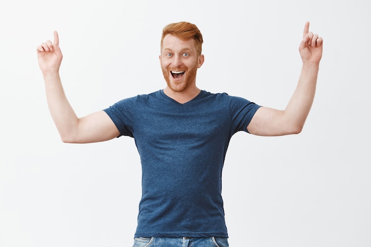 Zdarma Fotografie yeah we are winners. portrait of joyful celebrating male with ginger hair, bending and raising index fingers up in triumph gesture, grinning from happinesss and satisfaction, rejoicing from good news
