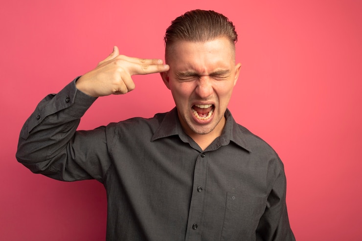 Zdarma Fotografie young handsome man in grey shirt making pistol gesture near his temple shouting crazy mad standing over pink wall