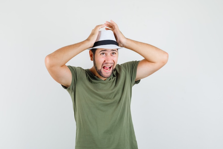 Zdarma Fotografie young male holding hands on head in green t-shirt, hat and looking helpless