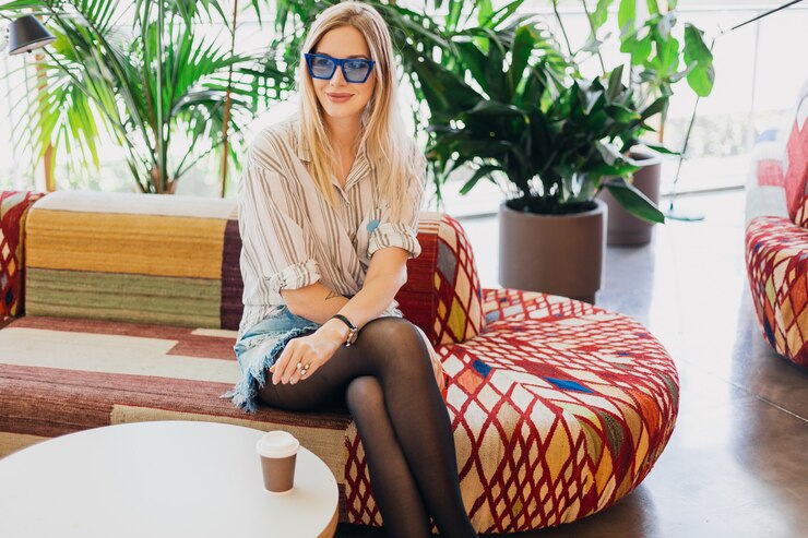Zdarma Fotografie young stylish smiling woman sitting in hipster cafe on sofa wearing shirt and blue sunglasses