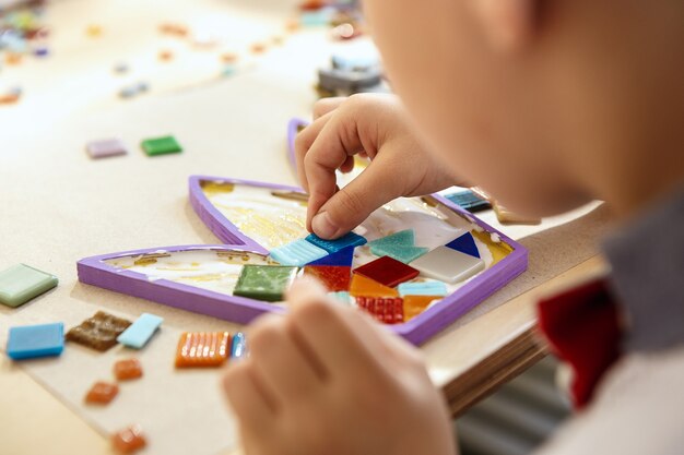 A arte do puzzle em mosaico para crianças, um jogo criativo para crianças. As mãos estão jogando mosaico na mesa. Detalhes coloridos multicoloridos close-up. Criatividade, desenvolvimento infantil e conceito de aprendizagem