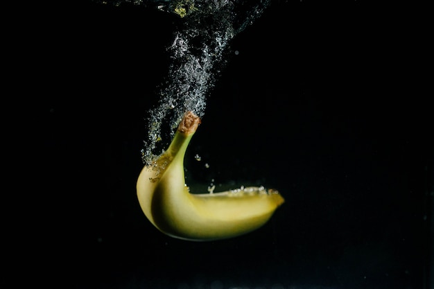 A banana amarela cai na água e borbulha em torno dela
