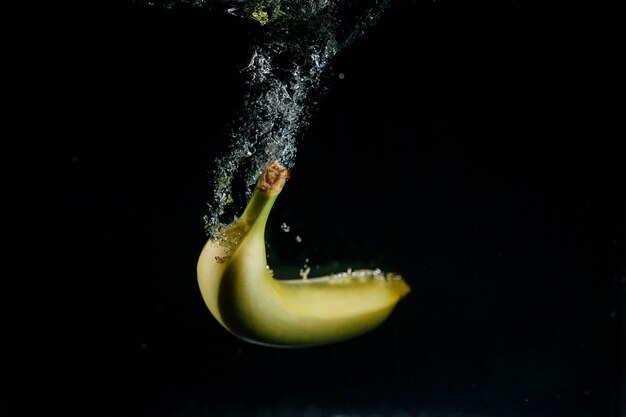 A banana amarela cai na água e borbulha em torno dela