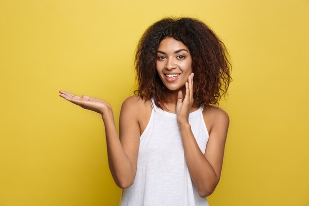 A bela e atrativa mulher afro-americana que publica joga com seus cabelos afro encaracolados. Fundo de estúdio amarelo. Espaço de cópia.