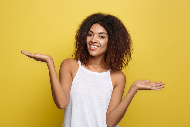 A bela e atrativa mulher afro-americana que publica joga com seus cabelos afro encaracolados. Fundo de estúdio amarelo. Espaço de cópia.