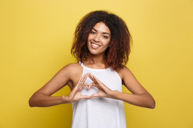 Foto grátis a bela e atrativa mulher afro-americana que publica joga com seus cabelos afro encaracolados. fundo de estúdio amarelo. espaço de cópia.