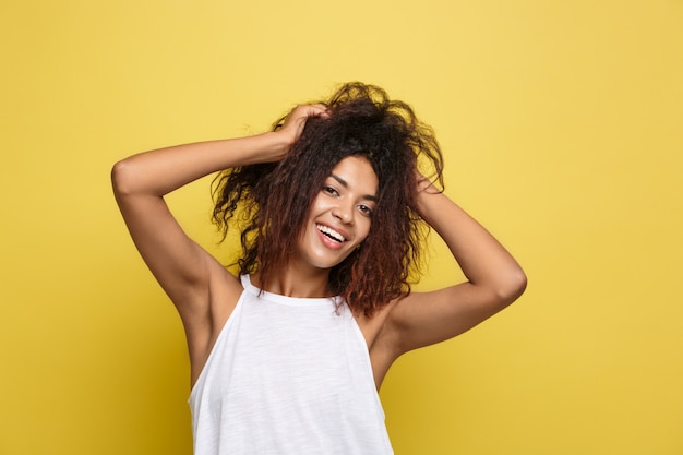 A bela e atrativa mulher afro-americana que publica joga com seus cabelos afro encaracolados. Fundo de estúdio amarelo. Espaço de cópia.