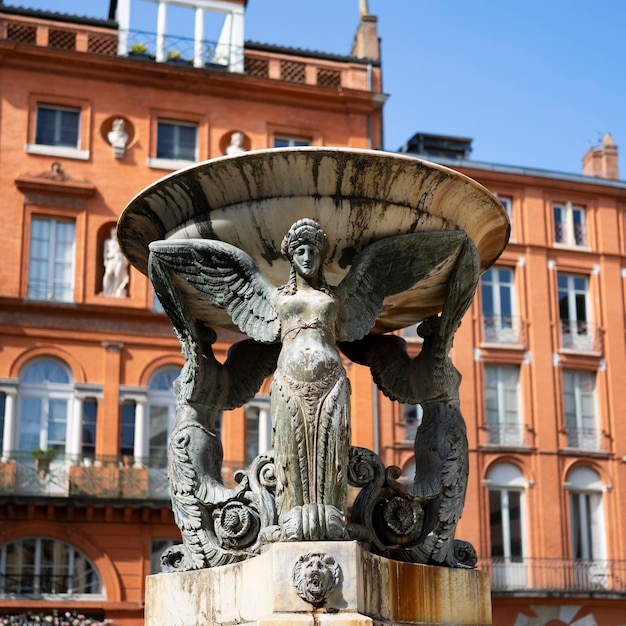 A bela fonte da Trindade da estátua no distrito histórico de Toulouse com construção de tijolos vermelhos no fundo França