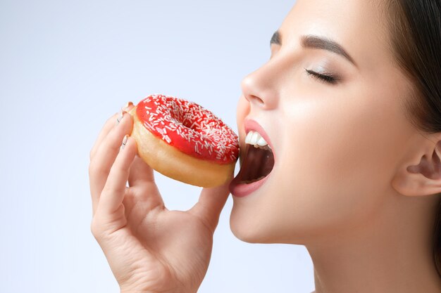 A bela mulher mordendo um donut no fundo cinza do estúdio