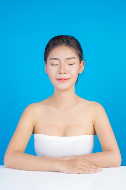 A beleza das mulheres com imagens perfeitas de saúde da pele Tocando em seu rosto e sorrindo como um spa para cuidar de sua pele Azul