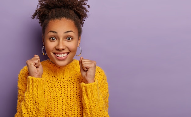 Foto grátis a campeã ou vencedora cerrou os punhos, alegra-se com o sucesso, sorri amplamente, mostra os dentes brancos, usa um macacão amarelo