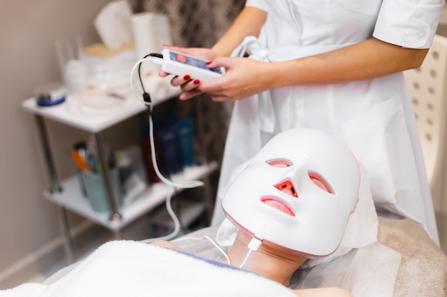 A cliente encontra-se no salão, na mesa de cosmetologia, com uma máscara branca no rosto