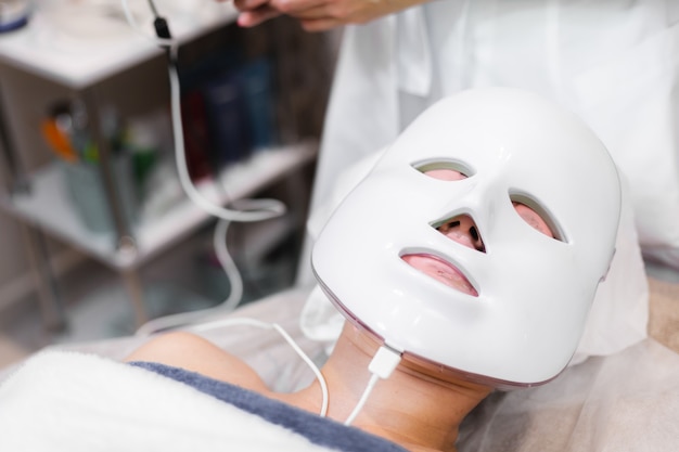 A cliente encontra-se no salão, na mesa de cosmetologia, com uma máscara branca no rosto