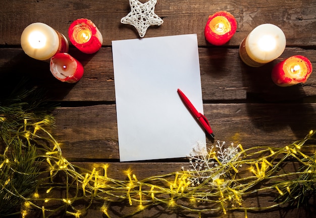 A folha de papel em branco na mesa de madeira com uma caneta e enfeites de natal.
