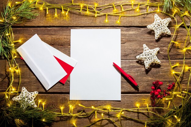 A folha de papel em branco na mesa de madeira com uma caneta e enfeites de Natal.