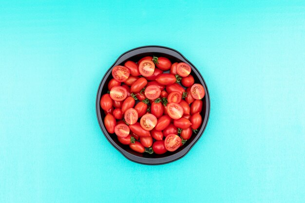 A frigideira cheia de tomate cereja no centro na superfície azul claro