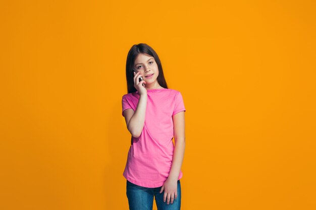 A garota adolescente feliz em pé e sorrindo contra laranja.