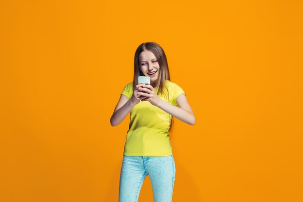 A garota adolescente feliz em pé e sorrindo contra um fundo laranja.