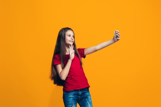 A garota adolescente feliz em pé e sorrindo contra um fundo laranja.