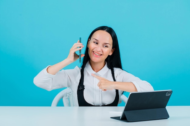 A garota blogueira sorridente está posando para a câmera do tablet segurando o telefone no fundo azul