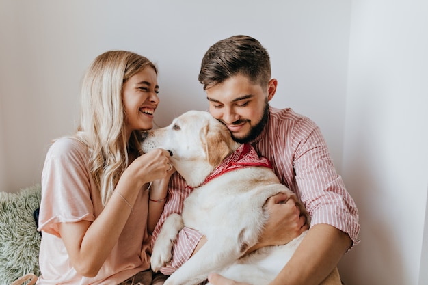 A garota com uma camisa enorme ri de todo o coração e olha para seu homem de cabelos escuros segurando labrador.