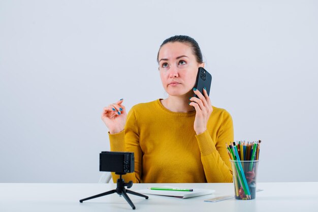 A garota do blogueiro está falando no telefone olhando para cima no fundo branco