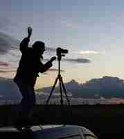 Foto grátis a garota no teto do carro fotografa o pôr do sol com um tripé