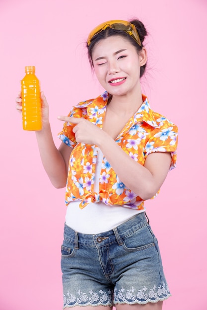 A garota tem uma garrafa de suco de laranja em um fundo rosa.