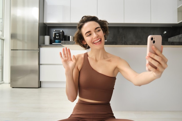 Foto grátis a imagem da jovem blogueira fitness registra seu treino em casa, bate-papos on-line enquanto faz ioga no bri