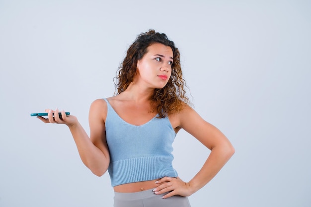 A jovem está olhando para a direita, colocando a mão na cintura no fundo branco