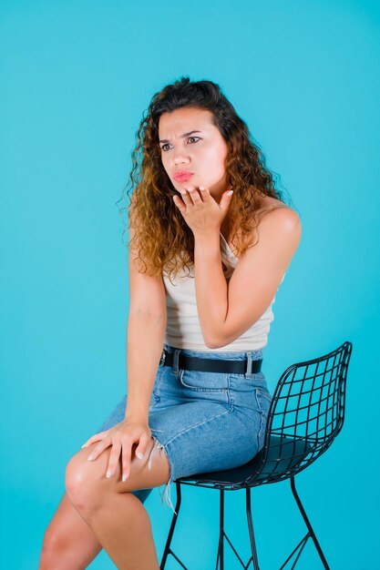 A jovem está segurando a mão sob o queixo, sentando-se no fundo azul