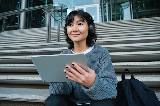 A jovem estudante asiática em fones de ouvido trabalha em artista digital remoto desenhando em tablet com gráfico