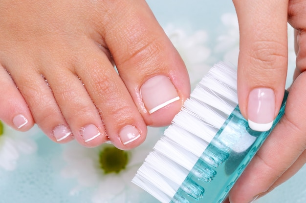 A jovem lava e limpa as unhas dos pés com água usando uma escova de limpeza