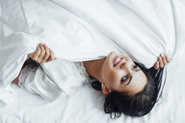 Foto grátis a jovem linda morena feliz encontra-se em sua cama acordando de manhã e suando.