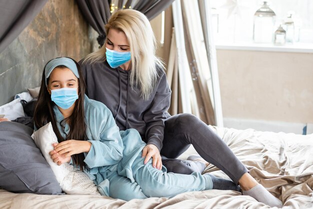 A jovem mãe afetuosa abraçando a filhinha, a família usando máscara facial médica, dando apoio, confortando, expressando amor. Conceito de coronavírus ou sintomas de doença pandêmica COVID-19.