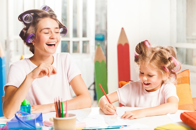 A jovem mãe e a filha pequena desenhando a lápis em casa