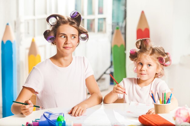 A jovem mãe e a filha pequena desenhando a lápis em casa