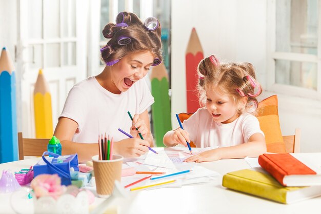 A jovem mãe e a filha pequena desenhando a lápis em casa