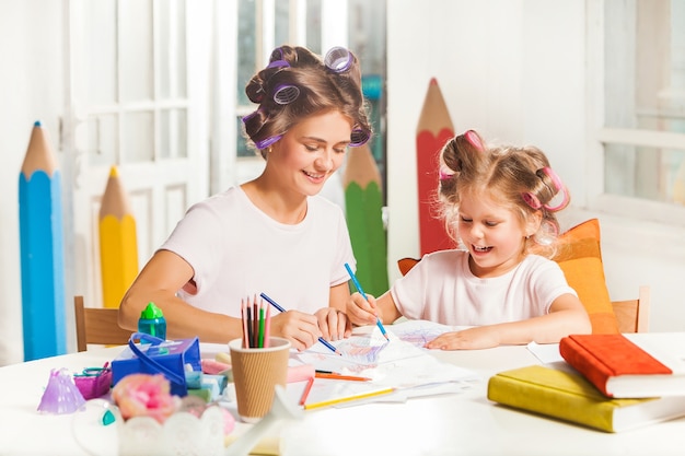 A jovem mãe e a filha pequena desenhando a lápis em casa