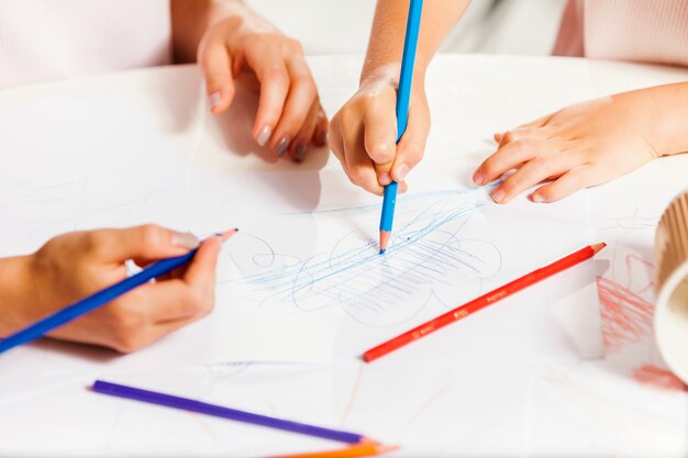 A jovem mãe e sua filha pequena desenhando com lápis em casa