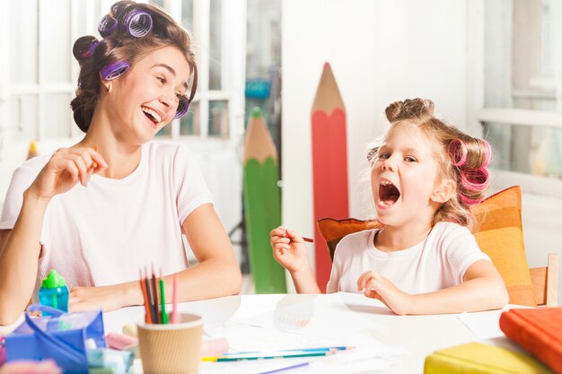 A jovem mãe e sua filha pequena desenhando com lápis em casa