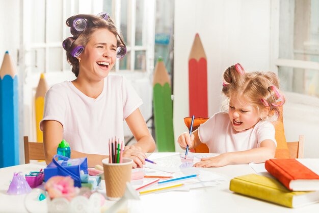 A jovem mãe e sua filha pequena desenhando com lápis em casa