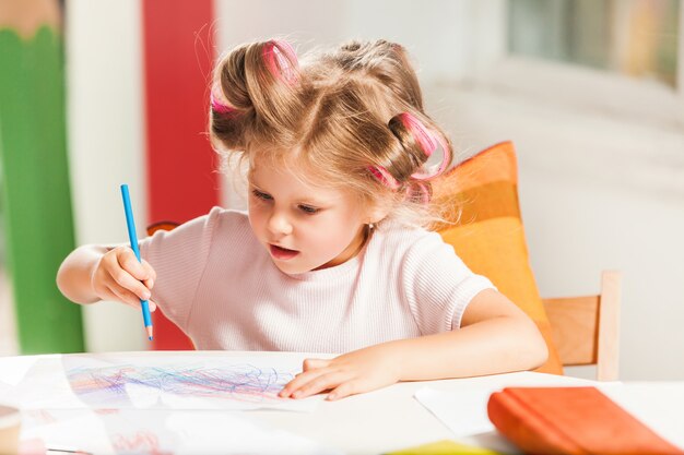 A jovem mãe e sua filha pequena desenhando com lápis em casa