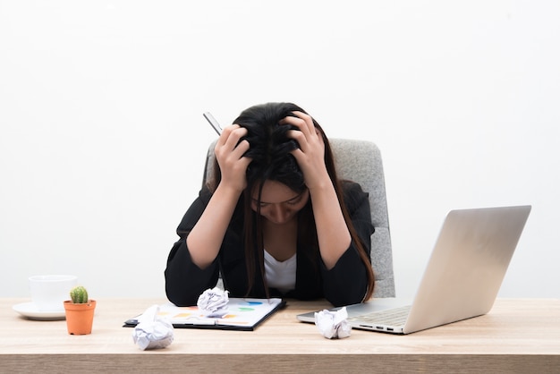 A jovem mulher de negócios segura sua cabeça e parece estressante com gráfico financeiro e laptop na mesa isolada no fundo branco