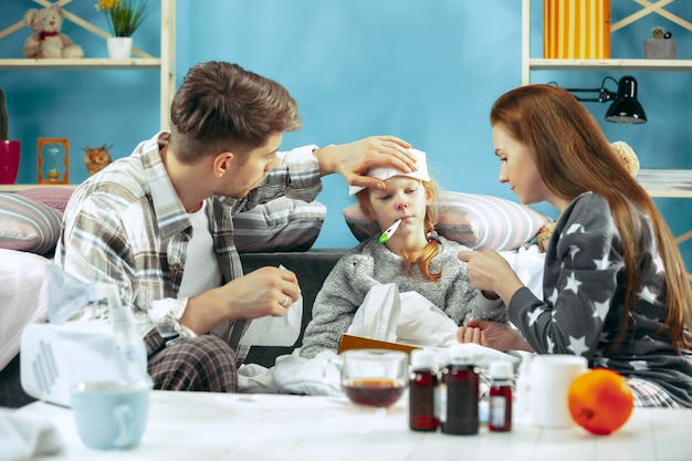 Foto grátis a jovem mulher e o homem com a filha doente em casa. tratamento em casa. lutando com uma doença. saúde médica. a ilusão familiar. o inverno, gripe, saúde, dor, paternidade, conceito de relacionamento