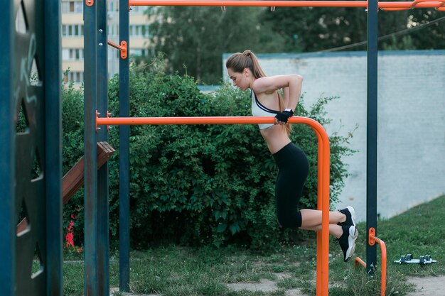 A jovem mulher forte e fisicamente cabida que faz o tríceps mergulha em barras paralelas no parque.